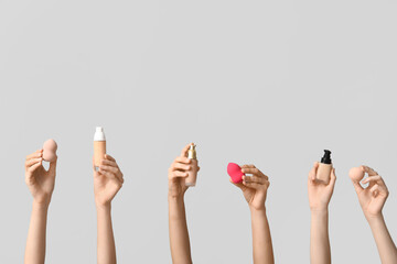 Female hands with bottles of makeup foundation and sponges on grey background