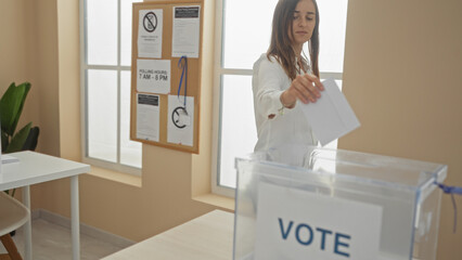 A young, attractive, caucasian woman votes in an indoor electoral college facility, casting her...