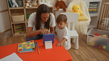 Woman and child engage with tablet indoors, surrounded by toys and learning materials, fostering education and connection in warm, cozy nursery setting.