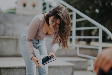 A young female student is engrossed in studying outdoors on stone stairs. She is focused on her...