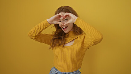 Beautiful young caucasian blonde woman making heart shape with hands over isolated yellow background