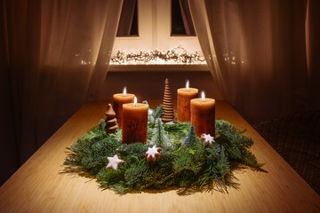 Fourth advent with burning orange brown candles on a wreath from green fir branches and Christmas...