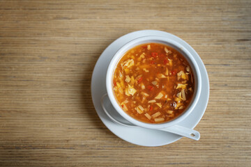 Chinese hot and sour soup from chicken stock with egg, meat and vegetables, white bowl with porcelain spoon on a wooden table in an Asian restaurant, top view from above, copy space