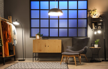 Interior of hall with glowing lamps, coat rack and armchair in evening