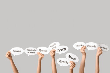 Female hands holding speech bubbles with text THANK YOU in different languages on grey background
