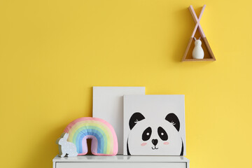 Cute picture with rainbow pillow on commode near yellow wall in children's room