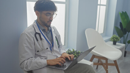 Handsome arab man in glasses and stethoscope using laptop in modern clinic office