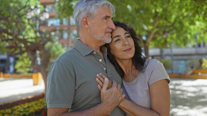 Middle age couple embracing lovingly in a sunny urban park, showcasing their strong relationship and the beauty of togetherness outdoors in a vibrant city setting.