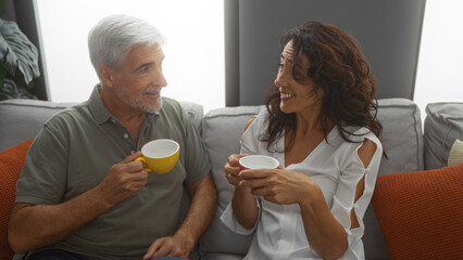 Middle-aged couple enjoying coffee together in a cozy living room, showcasing love and companionship in a homely indoor setting.