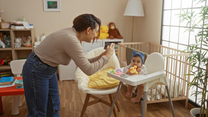 Woman photographing baby in cradle while standing in cozy bedroom; intimate mother-daughter moment full of love and warmth in stylish home interior.
