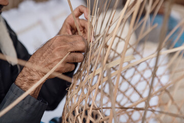 Old man is knitting weaving traditional basket from palm leaves, hands in frame