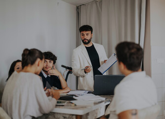 A group of high school students work together on assignments with their teacher in a warm, home-like environment, fostering a collaborative learning experience.