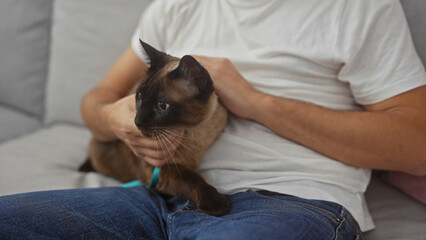 A man cuddling his siamese cat on a couch, illustrating companionship at home.