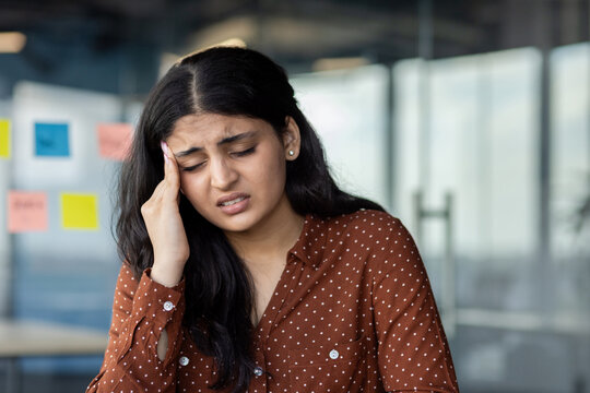 Latin American businesswoman with headache feeling stress while in office. She shows discomfort and contemplation, symbolizing work stress and health concerns.
