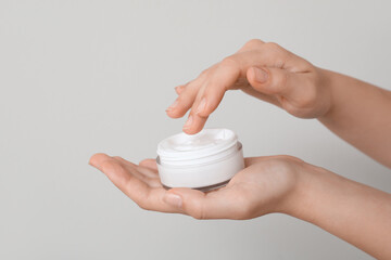 Female hands with jar of cosmetic cream on grey background