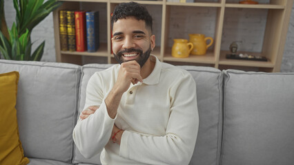 Handsome hispanic man smiling confidently while seated in a cozy modern living room.