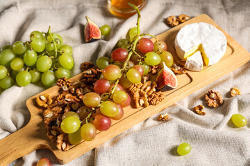 Wooden board with sweet ripe grapes, walnuts, fig and camembert cheese on napkin