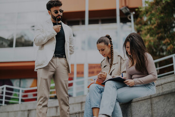 A group of students engaging in study outdoors in the city, taking notes and collaborating after...