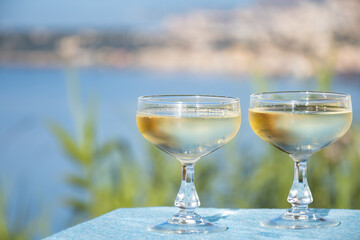 Sparkling wine, cava or champagne in two coupe glasses on table with view on Menton and Monte-Carlo, French Riviera, France is summer