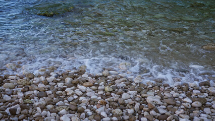 Colorful pebbles on a rocky beach with gentle ocean waves in a serene outdoor setting.