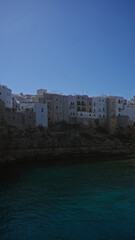 Naklejka premium Scenic view of the coastal town of polignano a mare in puglia, italy, showcasing its charming cliffside houses against a clear blue sky above the adriatic sea.