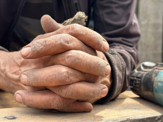 closeup of clasped rough dirty  hands of elderly hard working carpenter over wood plank 