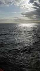 Ocean view under a cloudy sky with sun rays reflecting on the water creates a dramatic and serene atmosphere in the outdoor scene.