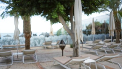 Fototapeta premium Blurred view of a tropical resort with defocused sun loungers, umbrellas, and palm trees in the background