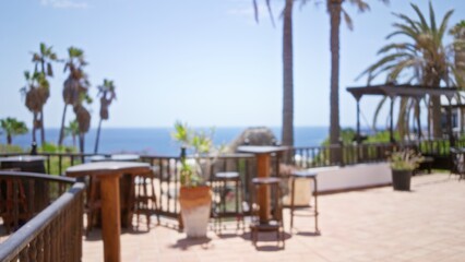 Blurry outdoor terrace scene with palm trees and ocean view in lanzarote, canary islands, spain, featuring defocused tables and chairs under a clear blue sky