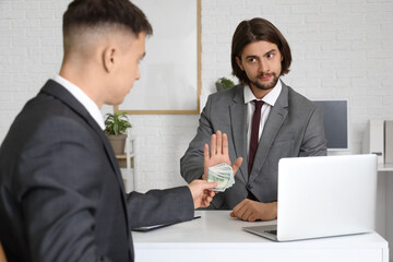 Obraz premium Young businessman refusing to take bribe at table in office. Corruption concept