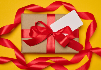 Box tied with red ribbon on yellow background, festive background