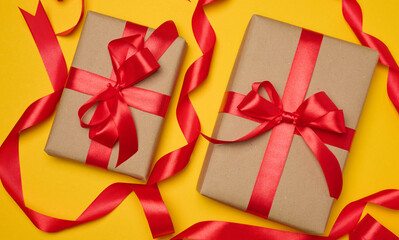 Two boxes tied with red ribbon on yellow background, festive background.