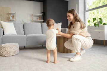 Cute baby girl learning to walk with mother at home