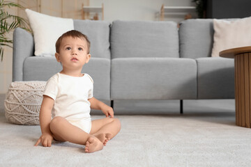 Cute baby girl in bodysuit sitting on carpet at home