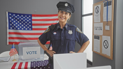 Smiling female police officer standing in an american voting station with flag and ballot box