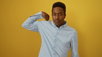 Young african american man makes a strength gesture on an isolated yellow background, displaying confidence and positivity.