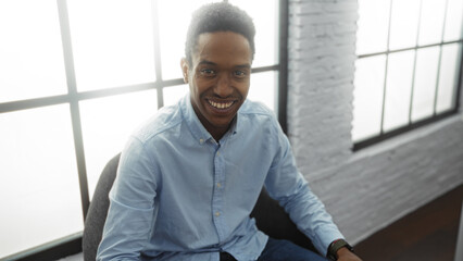 Young man smiling in modern office, showcasing positivity and professionalism in a bright workspace with large windows and stylish interior decor.