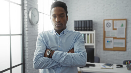 Young african american man standing confidently in modern office environment with arms crossed and...
