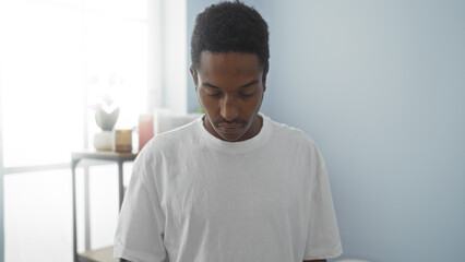 Young man in spa wearing white shirt standing in wellness room with soft lighting and calm atmosphere, capturing a moment of serene contemplation and self-care