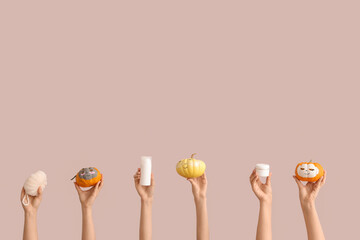 Female hands holding pumpkins with drawn faces, clay masks, bath sponge, bottle and jar of cosmetic products on pink background