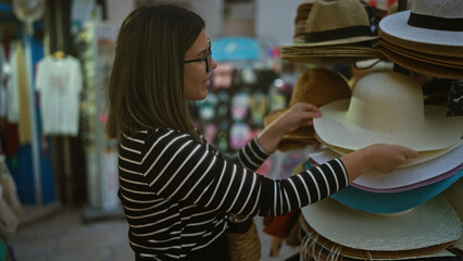 A young hispanic woman shops for hats in the picturesque streets of polignano a mare, italy,...