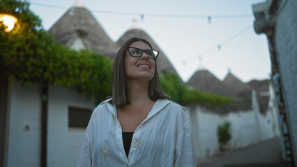 A young hispanic woman smiling and exploring the charming old town streets of alberobello, italy, known for its iconic trulli houses, in the beautiful region of puglia.