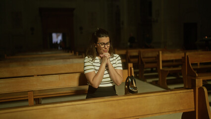 A young hispanic woman prays thoughtfully in a quiet church in italy, illuminated by soft light filtering through the window.