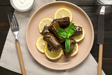 Plate with tasty Dolmas (stuffed grape leaves), lemon slices and cutlery on dark wooden background