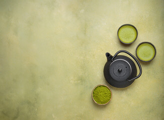 Matcha tea in cups, black iron teapot and matcha powder on a green background, a relaxing and...