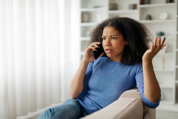 Fototapeta premium Distressed African American woman have phone conversation, sitting on the sofa at home. High quality photo