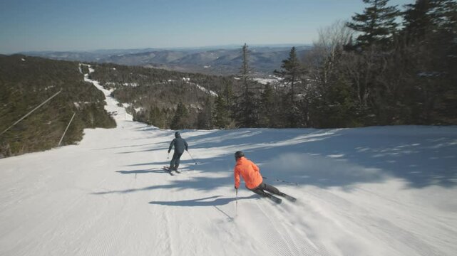 4K video of a couple man and woman skiers alpine skiing on cold winter snow at a ski resort mountain with sunshine. Adventure and thrill while on vacation and holiday. Killington, Vermont, USA.