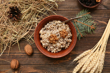 Bowl of traditional Ukrainian Kutya dish with wheat, pine cone and Christmas tree branch on wooden background