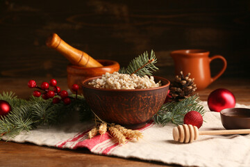 Bowl of traditional Ukrainian Kutya dish with fir branches and Christmas balls on wooden background