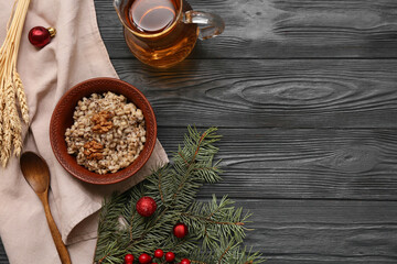 Bowl of traditional Ukrainian Kutya dish with Christmas tree branches and jug of uzvar on black wooden background